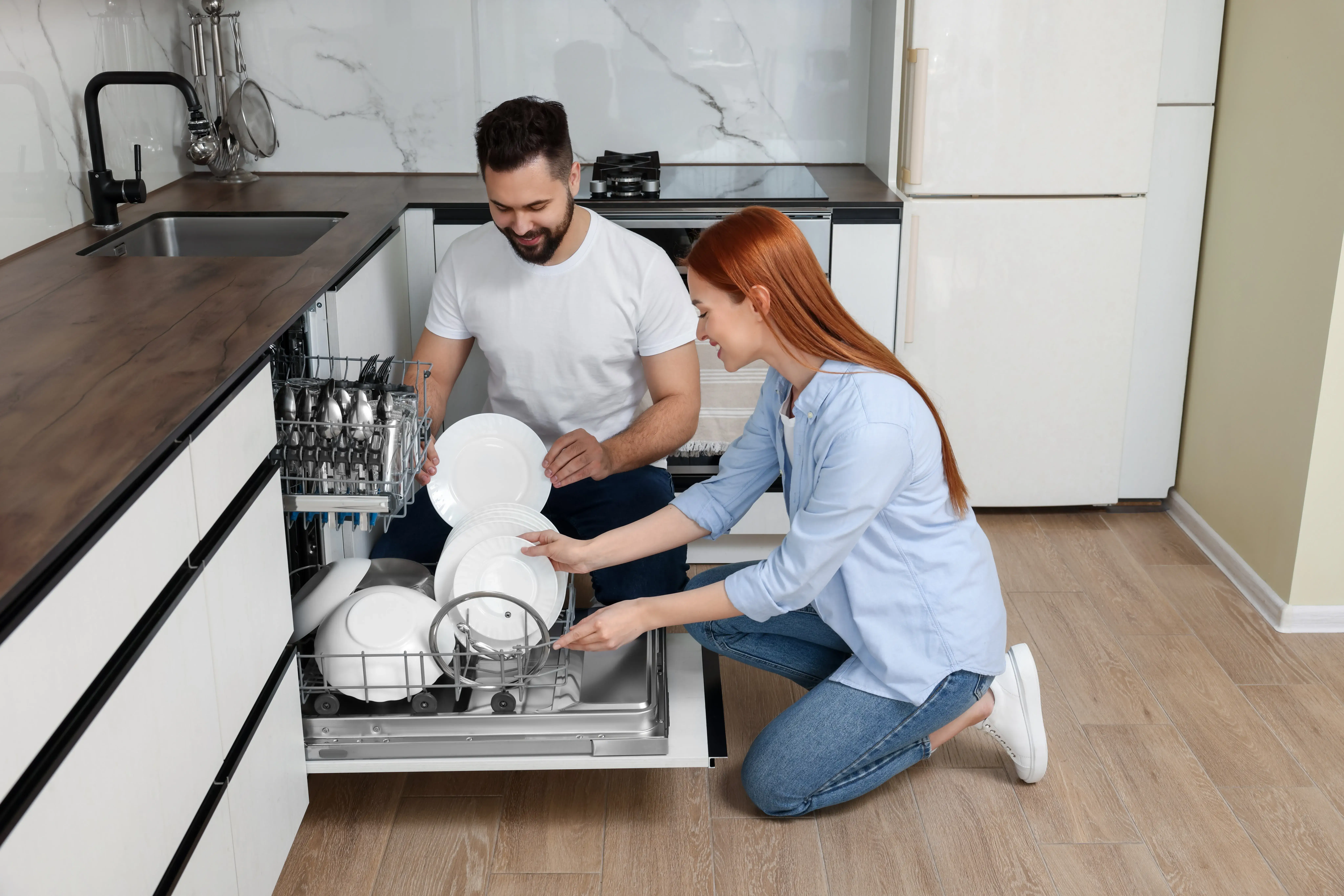 Casal carregando a lava-louças com pratos em uma cozinha moderna.